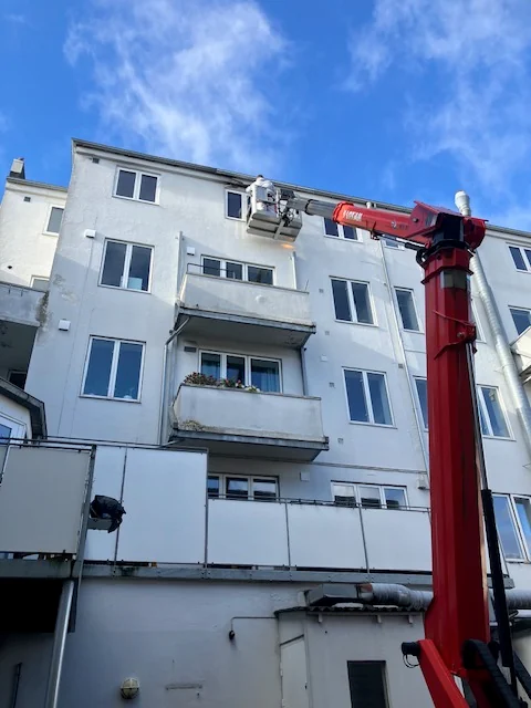 Lys etageejendom med altaner og rød lift ved facaden