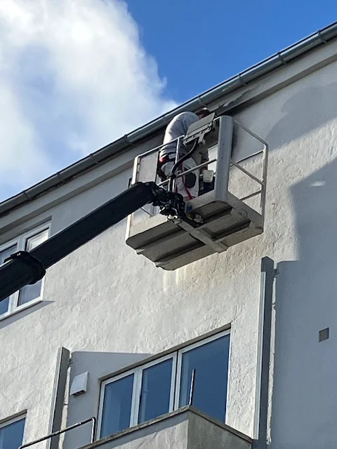 Maler i lift ved tagkanten på en lys facade
