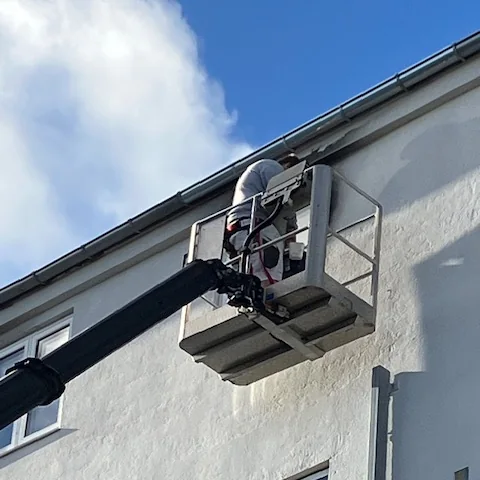Maler i lift arbejder ved tagkanten på en lys facade